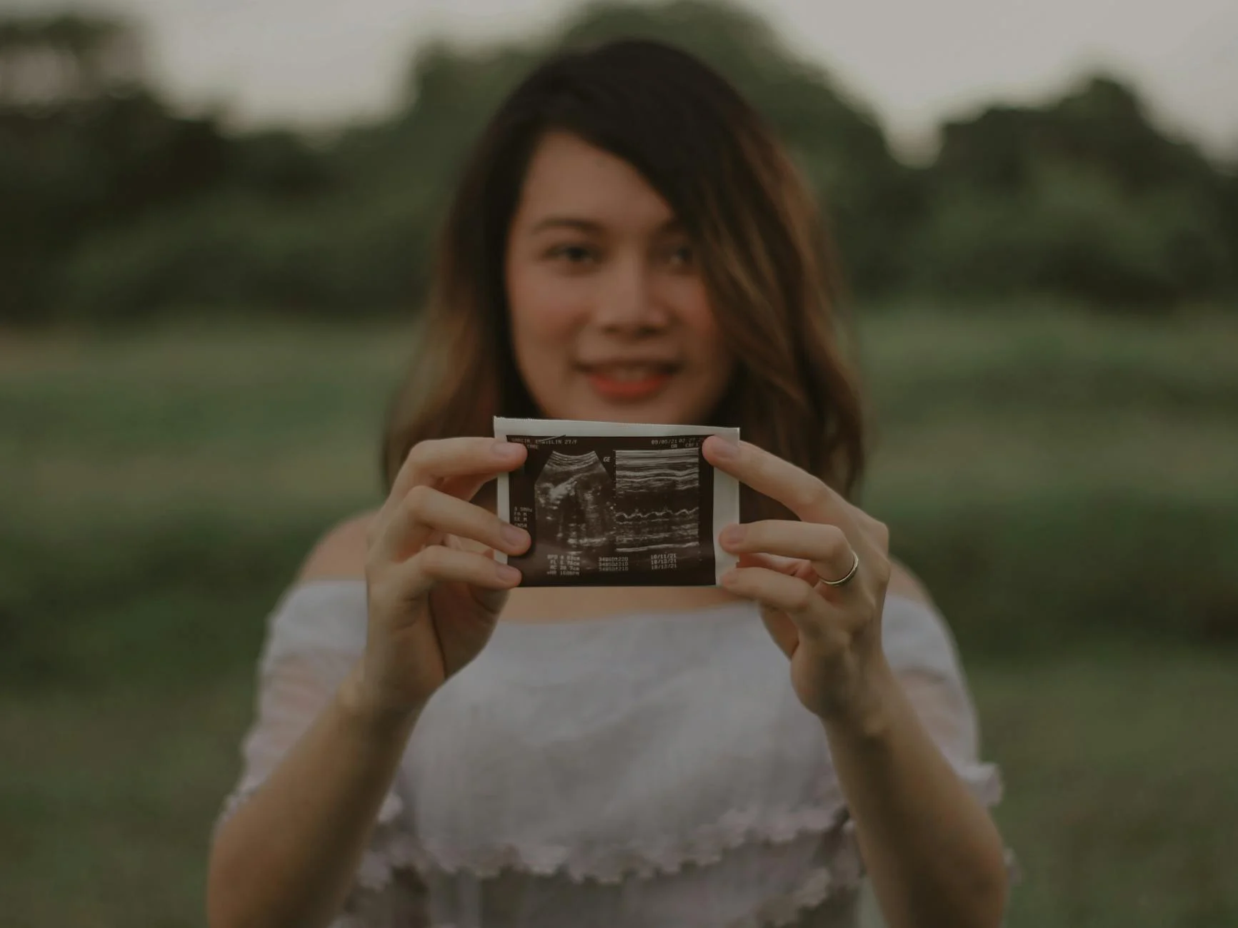 Eine schwangere Frau hält ein Ultraschallbild in den Händen und lächelt, während sie ihren Babybauch berührt – symbolisiert die Freude und Verbindung während der Schwangerschaft.