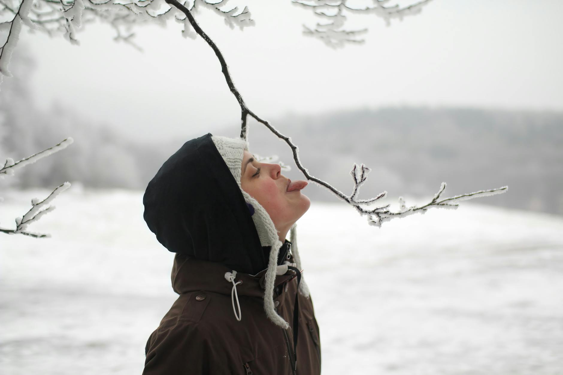 Eine Frau mit warmen Socken und einer Tasse Tee sitzt entspannt auf einem Sofa und hält ihre Füße auf einem Kissen, während draußen winterliches Wetter zu sehen ist.