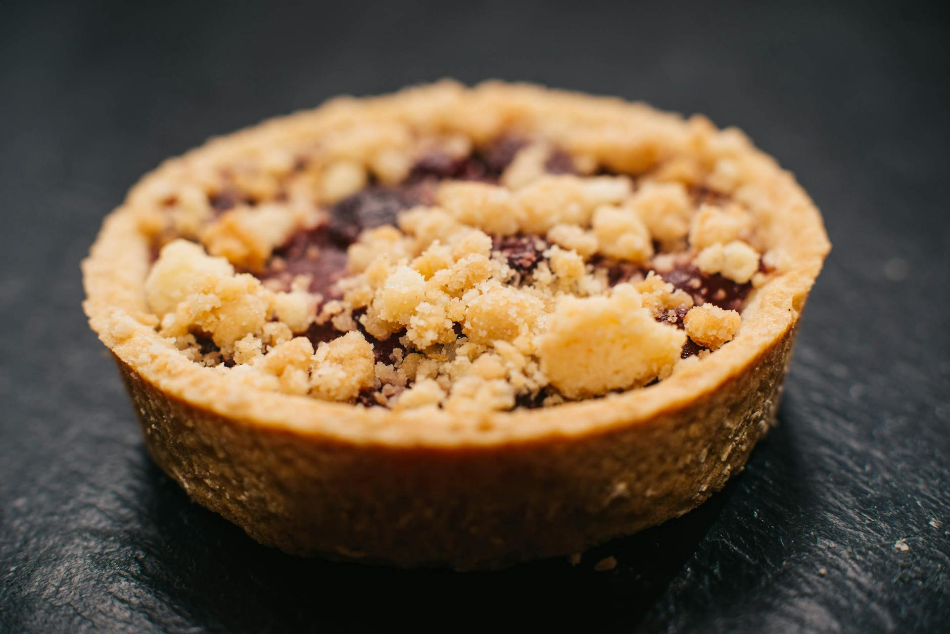 Ein frisches, gesundes Dessert in einem Glas, bestehend aus Schichten von Avocado-Mousse, Beeren und Hafercrumble, natürlich beleuchtet auf einem Holztisch mit einfachen Küchenutensilien im Hintergrund.